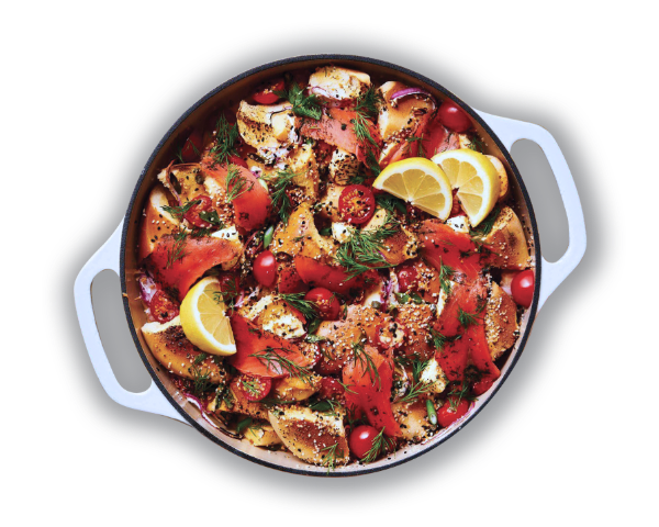 A round dish with bagel pieces, smoked salmon, cherry tomatoes, lemon wedges, and dill. The food is seasoned with black pepper and displayed in a gray pot with handles. GREENHOUSE Goodness A round dish with bagel pieces, smoked salmon, cherry tomatoes, lemon wedges, and dill. The food is seasoned with black pepper and displayed in a gray pot with handles. GREENHOUSE Goodness