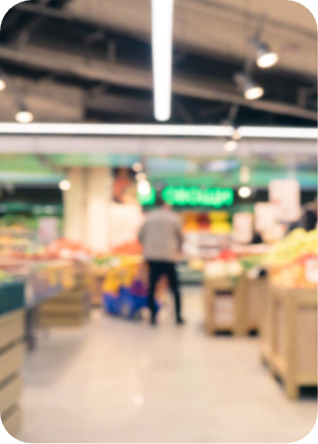 Blurred image of a person standing with a shopping cart in a grocery store aisle, surrounded by shelves and bins stocked with various products. Bright overhead lighting and a green sign are visible in the background. GREENHOUSE Goodness Blurred image of a person standing with a shopping cart in a grocery store aisle, surrounded by shelves and bins stocked with various products. Bright overhead lighting and a green sign are visible in the background. GREENHOUSE Goodness
