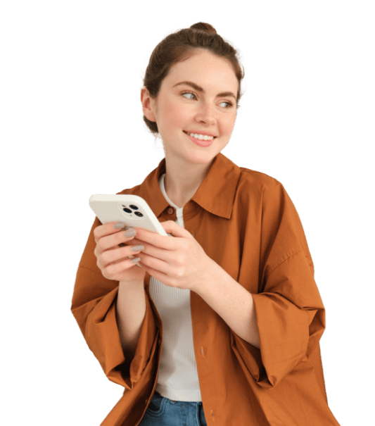 A person with short hair is smiling and looking to the side while holding a smartphone. They are wearing a white shirt and an open, brown button-up shirt over it. The background is plain white. GREENHOUSE Goodness A person with short hair is smiling and looking to the side while holding a smartphone. They are wearing a white shirt and an open, brown button-up shirt over it. The background is plain white. GREENHOUSE Goodness