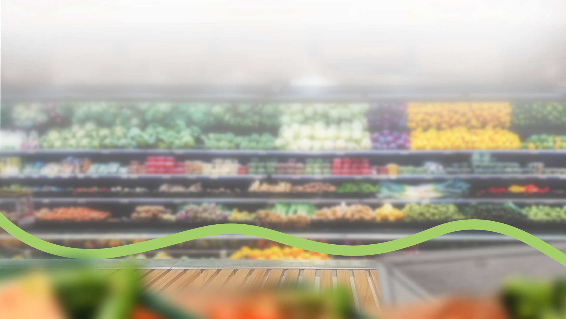 A blurred supermarket produce section with various fruits and vegetables on display. A wavy green line runs horizontally across the lower part of the image. GREENHOUSE Goodness